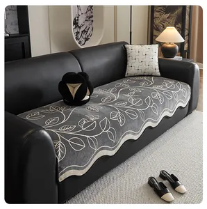 Detail of grey chenille sofa cover with floral pattern and scalloped edges on leather sofa
