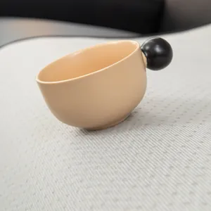 Mug en céramique beige avec poignée sphérique noire sur tissu texturé moderne