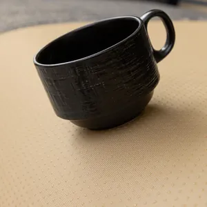 Moderne schwarze Keramiktasse mit gerippter Textur und mattem Finish auf einer beigen Matte
