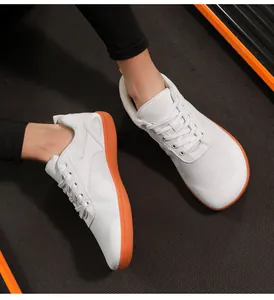 Close-up of white mesh barefoot shoes with bright orange soles on a textured black floor