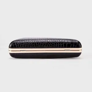 Detailed view of crocodile pattern embossed on a black evening clutch with gold metal frame