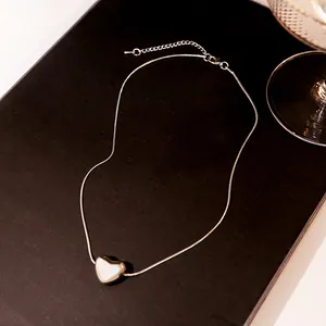 Close-up of silver snake chain necklace featuring a heart pendant with white shell inlay