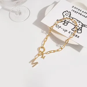 Macro detail of gold link chain with double M pendant featuring crystal pave and smooth finish