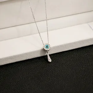 Close-up of a silver-toned necklace featuring an evil eye disc and teardrop pendant