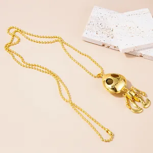 Detail of gold-colored round bead chain with cute skull robot pendant on beige background