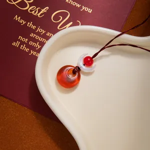 Detail of red agate peace buckle pendant with white crescent bead on woven cord