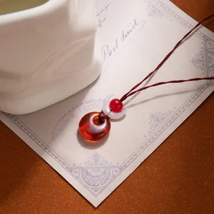 Detail of red circular pendant with half-moon bead on dark red braided cord necklace