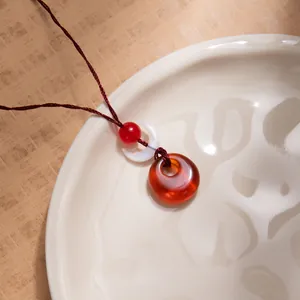 Detail view of a pendant necklace with a translucent ring and crescent on a ceramic tray