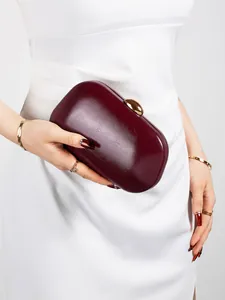 Macro shot of deep burgundy clutch bag with elegant gold pebble clasp detail