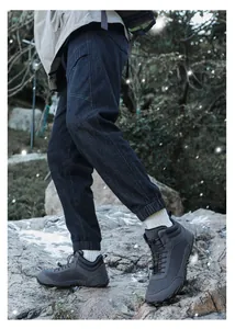 Πλάγια όψη σκούρων γκρι αδιάβροχων μποτών πεζοπορίας σε βράχια στο δάσος