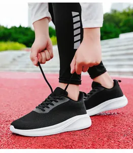 Gros plan de chaussures de running en mesh noir respirant sur piste rouge avec semelles blanches