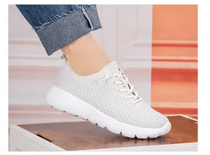 Close-up of beige knit breathable sneakers on feet with rolled-up dark denim jeans