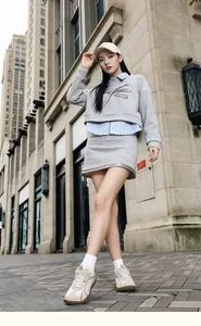 Detalle de sudadera corta gris con lazo de cadena y camisa a rayas azules