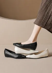 Detailed close-up of retro pointed-toe flats in black and beige with gold emblem details