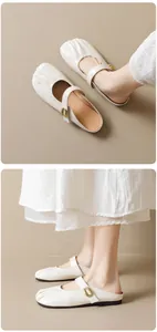 Close-up detail of cream Mary Jane mules featuring pleated toe and gold oval metal buckle