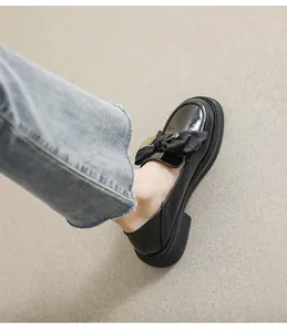 Detalle de mocasines con plataforma de charol negro con lazo y hebilla metálica dorada