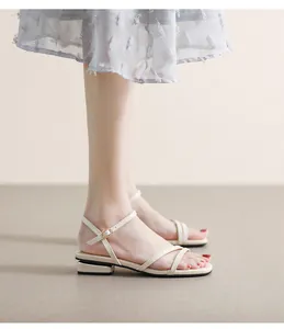 Detalle de sandalias planas crema con correas cruzadas y decoración metálica en tacón
