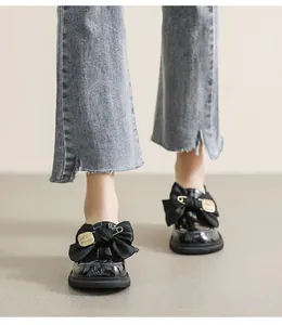 Primer plano de mocasines de charol negro con lazo y accesorio de alfiler dorado
