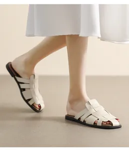 Detail of cream woven leather flat sandals styled with a white dress in a minimalist setting