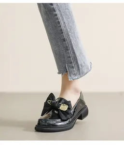Detalle de mocasines de charol negro con lazo de tela grande y detalle de imperdible dorado