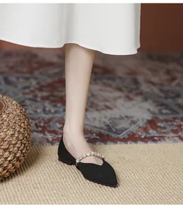 Close-up of black pointed-toe flat shoe with pearl strap on foot with white dress