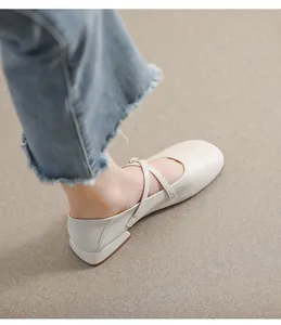 Detaillierte Draufsicht auf cremefarbene Mary Jane Schuhe mit gekreuzten Riemen auf Sand