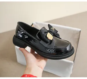Vista detallada de mocasines de charol negro con lazo decorativo y hebilla dorada