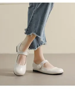 Detail view of cream Mary Jane flats with round toe and strap on blue denim jeans
