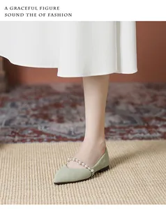 Close-up of green pointed-toe flat shoes with elegant pearl strap on fabric surface