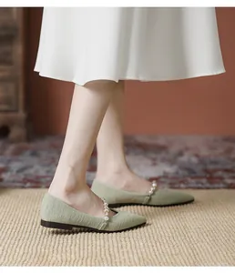 Detail view of light green pointed-toe flat shoes with pleated texture and pearl strap