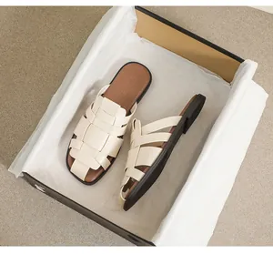 Top view of beige woven flat mules with square toe design and branded packaging box