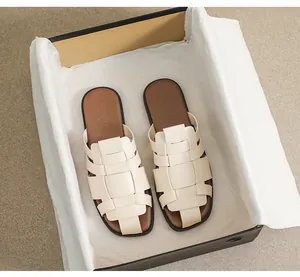 Detailed view of woven beige flat slide sandals presented in a premium black gift box