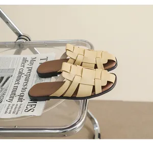Detail of beige woven leather flat mules on a modern chair with newspaper decor