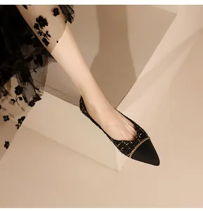 Detail of pointed-toe flats in black tweed fabric with elegant gold chain decoration