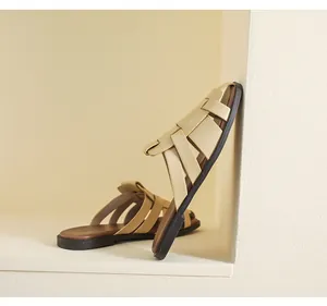 Detail of beige woven cross strap leather flat mules with brown sole in minimalist setting