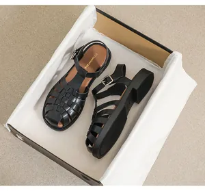 Detailaufnahme von schwarzen gewebten Leder-Römersandalen in einem Schuhkarton