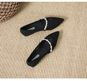 Detailed view of pointed black flats with decorative pearl strap on woven mat