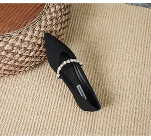 Top view of black pointed toe flat shoes with elegant pearl strap on woven texture mat