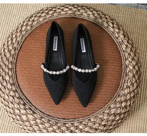 Detailed top view of black pointed-toe ballet flats with decorative pearl strap on woven mat