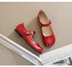 Overhead view of red patent leather Mary Jane flats with round toe on beige textured surface