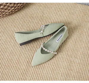 Detailed top view of light green pointed flats with pearl strap on a natural woven mat