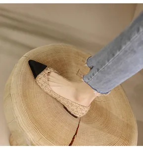 Detail of pointed-toe flats featuring black tip and beige woven texture on wooden stool