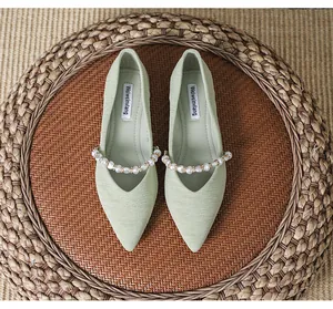 Close-up of light green pointed ballet flat with elegant pearl strap and textured fabric