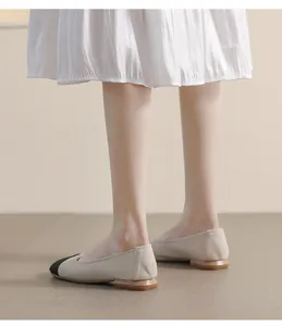 Close-up of beige lychee leather flats with black cap toe and wood grain low heel
