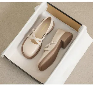 Detail view of cream Mary Jane shoes featuring crossover straps and golden metal buckles