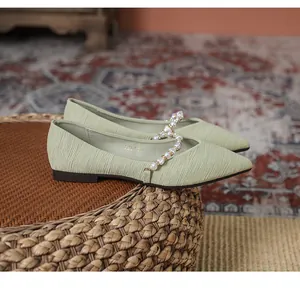 Detail of light green pointed toe flats featuring a pearl strap and textured fabric
