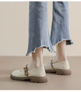 Detail view of off-white Mary Jane shoes with brown bow and pearl accent on platform sole