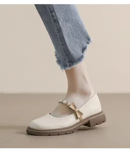 Detail of beige Mary Jane platform shoe with bow, pearl strap, and brown rubber sole