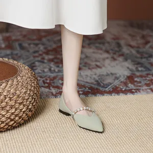 Elegant pointed toe sage green flat shoes with pearl strap shown on feet in stylish room