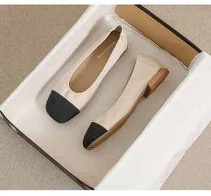 Detailed top view of beige flat shoes with black toe caps in a premium packaging box